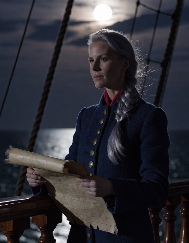 A silver-haired navigator in a navy wool coat holds a sea chart at a ship's rail under a full moon.